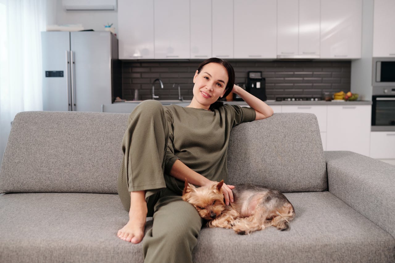 A woman relaxing with her Yorkshire Terrier on a cozy sofa in a modern kitchen setting.